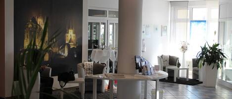 A modern hotel lobby with a large painting of a cityscape, a round white table, and comfortable seating areas.