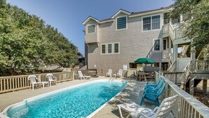 Uma casa de dois andares com piscina, espreguiçadeiras e um terraço coberto.