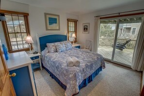 A bedroom with a large bed, two bedside tables, a desk, and a view of the balcony.
