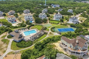 A residential area with multiple houses, a swimming pool, tennis courts, and a large water tower in the background.