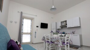 Un espacio habitable compacto con kitchenette, zona de comedor con mesa y sillas, y sofá con funda azul.