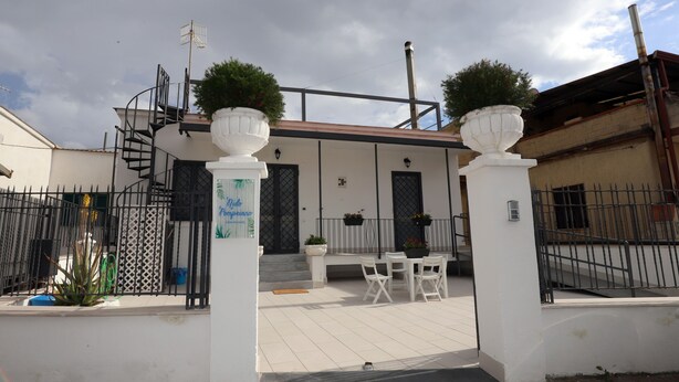 Un edificio blanco con un patio techado, una escalera y una valla metálica.