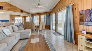 Un vaste espace de vie doté d’un plafond en bois, d’une table à manger avec des chaises, d’un canapé et d’un téléviseur posé sur un meuble en bois.