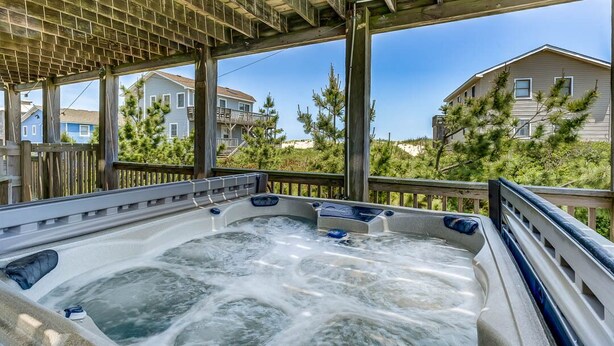Un bain à remous avec une terrasse en bois et une vue sur les maisons et les arbres.