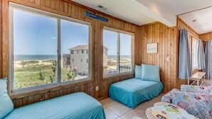 Une chambre avec deux lits, une petite table et de grandes fenêtres donnant sur la plage et l’océan.
