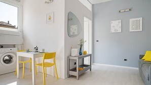 A modern kitchen with a washing machine, a dining table with yellow chairs, and a grey sofa with a yellow pillow. - GuestHost - The apartment is located in a quiet area, in a closed / private street overlooking the green and private gardens.It is located in a strategic position, a few steps from the historic center (the main road is located in absolute proximity to on (Bologna)