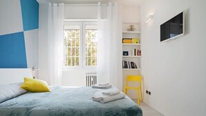 A bedroom with a bed, a window, a bookshelf, a chair, and a TV. - GuestHost - The apartment is located in a quiet area, in a closed / private street overlooking the green and private gardens.It is located in a strategic position, a few steps from the historic center (the main road is located in absolute proximity to on (Bologna)