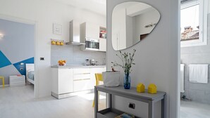 A modern kitchen with white cabinets, a microwave, and a stove. There's a dining area with a grey console table and a mirror above it. - GuestHost - The apartment is located in a quiet area, in a closed / private street overlooking the green and private gardens.It is located in a strategic position, a few steps from the historic center (the main road is located in absolute proximity to on (Bologna)