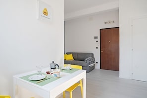 A dining area with a table set for two, a sofa, and a door in the background.