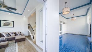 A modern living room with a sofa, a staircase, and a pool area with blue tiles. - hung hoang villa hoi an (Tp. Hội An)