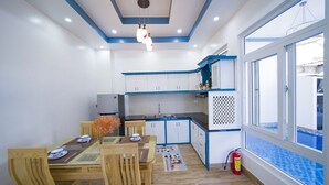 A compact kitchen with white cabinets, a dining table with chairs, and a window overlooking a blue-tiled area. - hung hoang villa hoi an (Tp. Hội An)