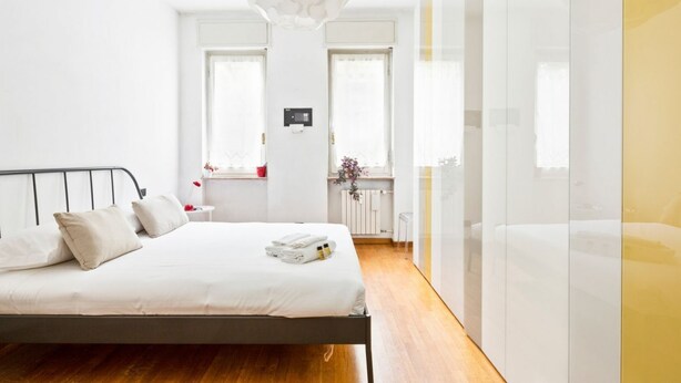 A modern bedroom with a bed, bedside table, and a window. - GuestHost - NEW! Two-room apartment one step away from SAN SIRO STADIUM! (Milano)