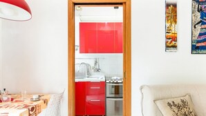 A room with a dining table, a sofa, a kitchen with red cabinets, and a door leading to another room. - GuestHost - NEW! Two-room apartment one step away from SAN SIRO STADIUM! (Milano)