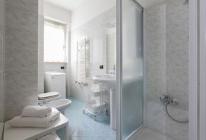 Un baño con inodoro, bidé, lavamanos y ducha.