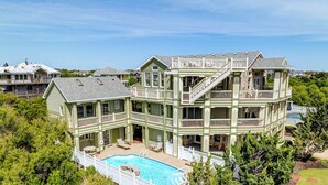 Une grande maison à plusieurs étages, dotée d’une piscine et de nombreux balcons.