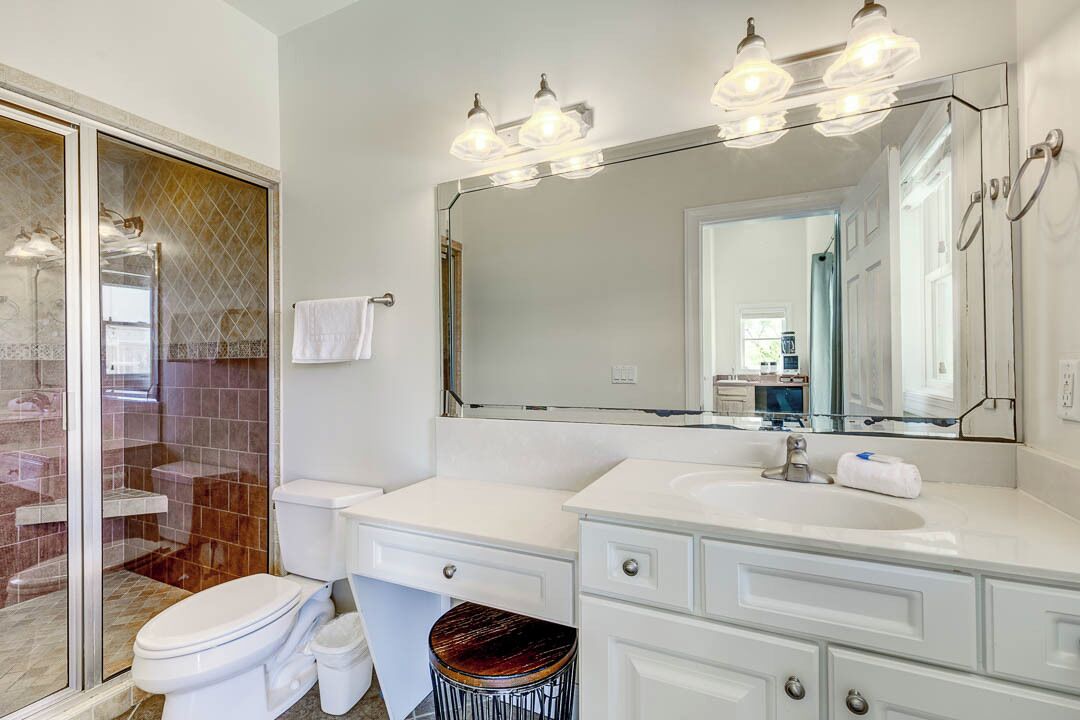 A modern bathroom with a glass shower enclosure, a large mirror, and a white vanity with a sink and countertop.