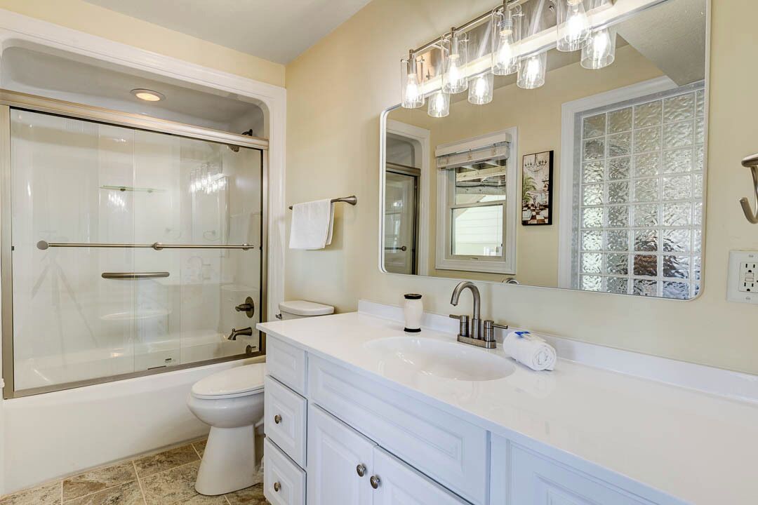 A modern bathroom with a glass-enclosed shower, a white sink, and a large mirror with lights above.