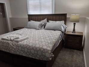 A neatly made bed with patterned bedding, a bedside lamp, and a nightstand with a drawer. - Doctor's Lounge - An Executive Home in Niagara (St. Catharines)
