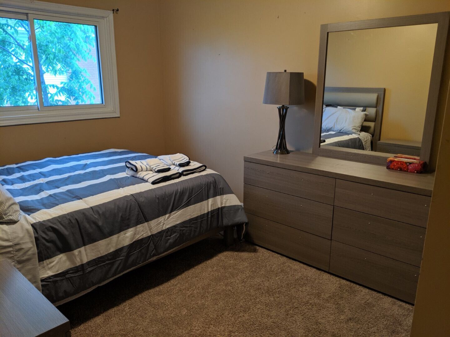 Une chambre à coucher avec un lit, une commode, un miroir et une fenêtre.