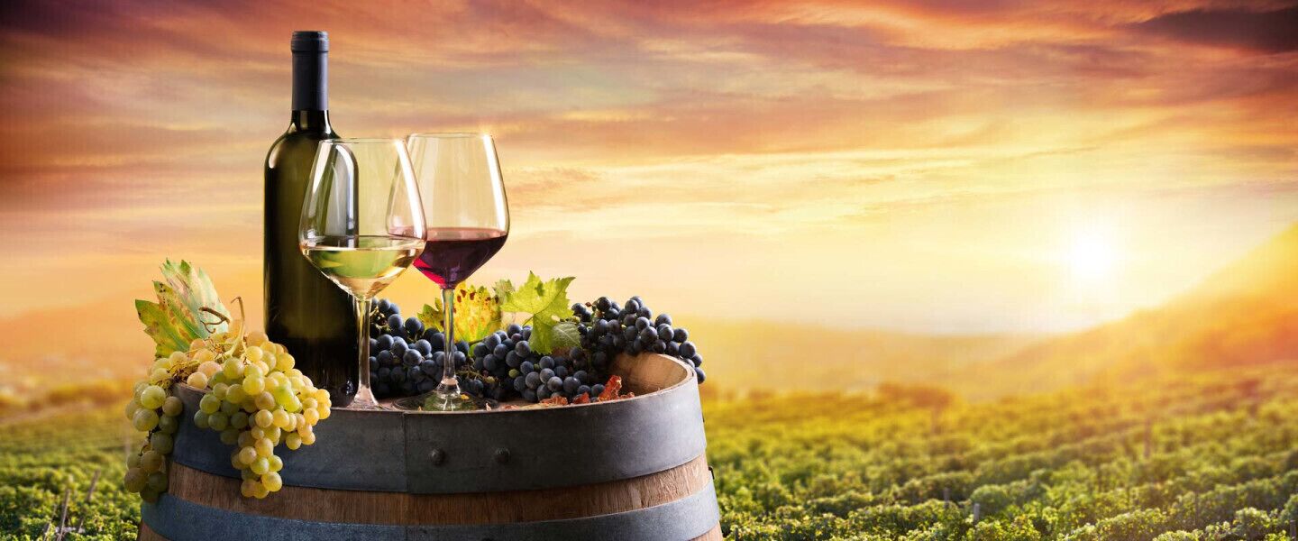 A wine barrel with a bottle and glasses, surrounded by grapes and leaves, set against a sunset background.