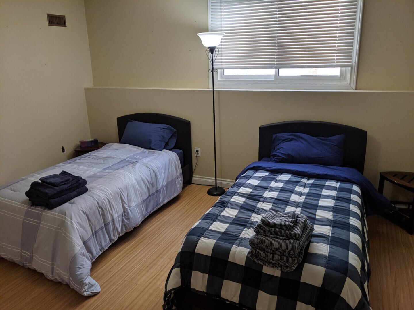 Un dormitorio con dos camas, una lámpara de pie y una ventana con persianas.