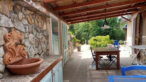 Un patio exterior cubierto con pared de piedra, una fuente de terracota, una mesa de madera y sillas azules.