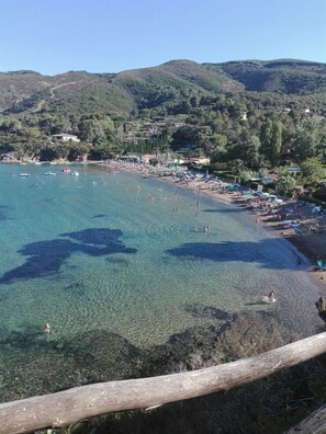 Une plage côtière aux eaux limpides, bordée d’un rivage sablonneux, avec des collines en arrière-plan.