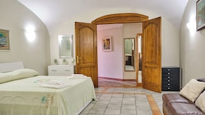 Un dormitorio con una cama, un aparador, un sofá de cuero marrón y una puerta de madera que da a otra habitación.