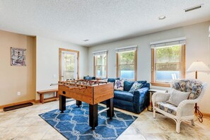 A room with a foosball table, a blue sofa, a wicker armchair, and large windows. - The Big Easy | 805 ft from the beach | Private Pool, Hot Tub, Dog Friendly | Duck (Duck)