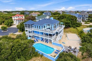 A large two-story house with a pool, multiple decks, and a beach area.