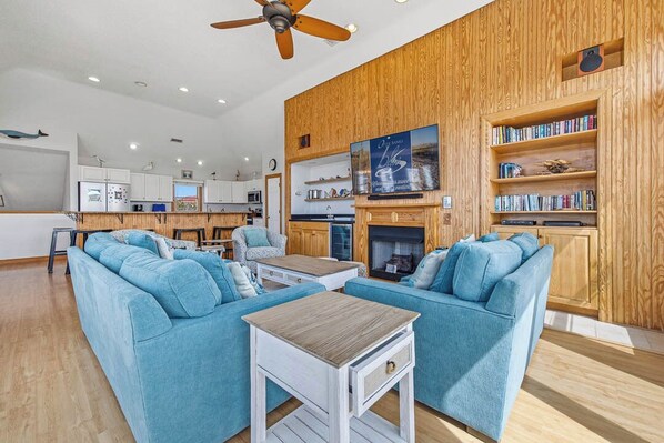 A modern living room with blue sofas, a wooden accent wall, a fireplace, and a bookshelf.
