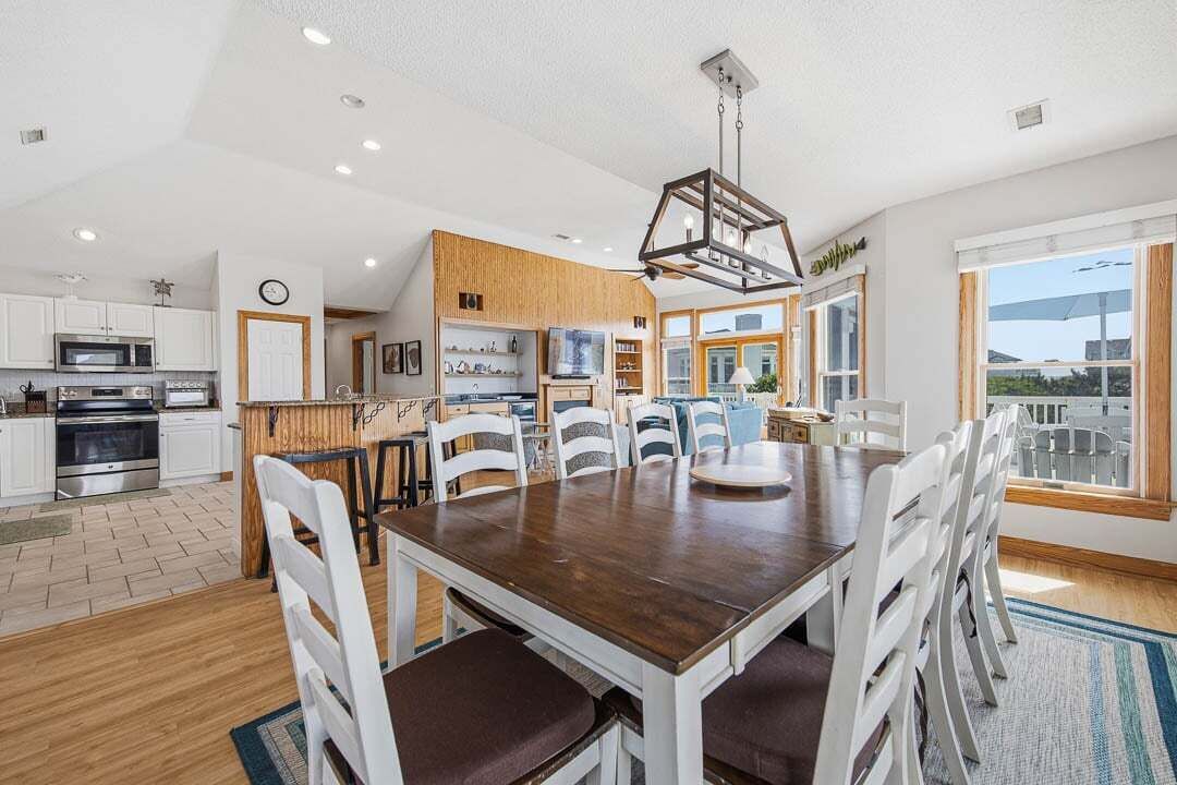 A modern kitchen with white cabinets, a wooden dining table, and a large window.