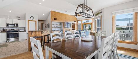 A modern kitchen with white cabinets, a wooden dining table, and a large window.