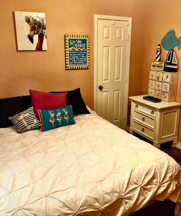 A bedroom with a bed, pillows, a dresser, a door, and wall decorations. - Turtle Cove - 3 Bedroom / 2 Bathroom / Sleeps 9 (Crystal Beach)