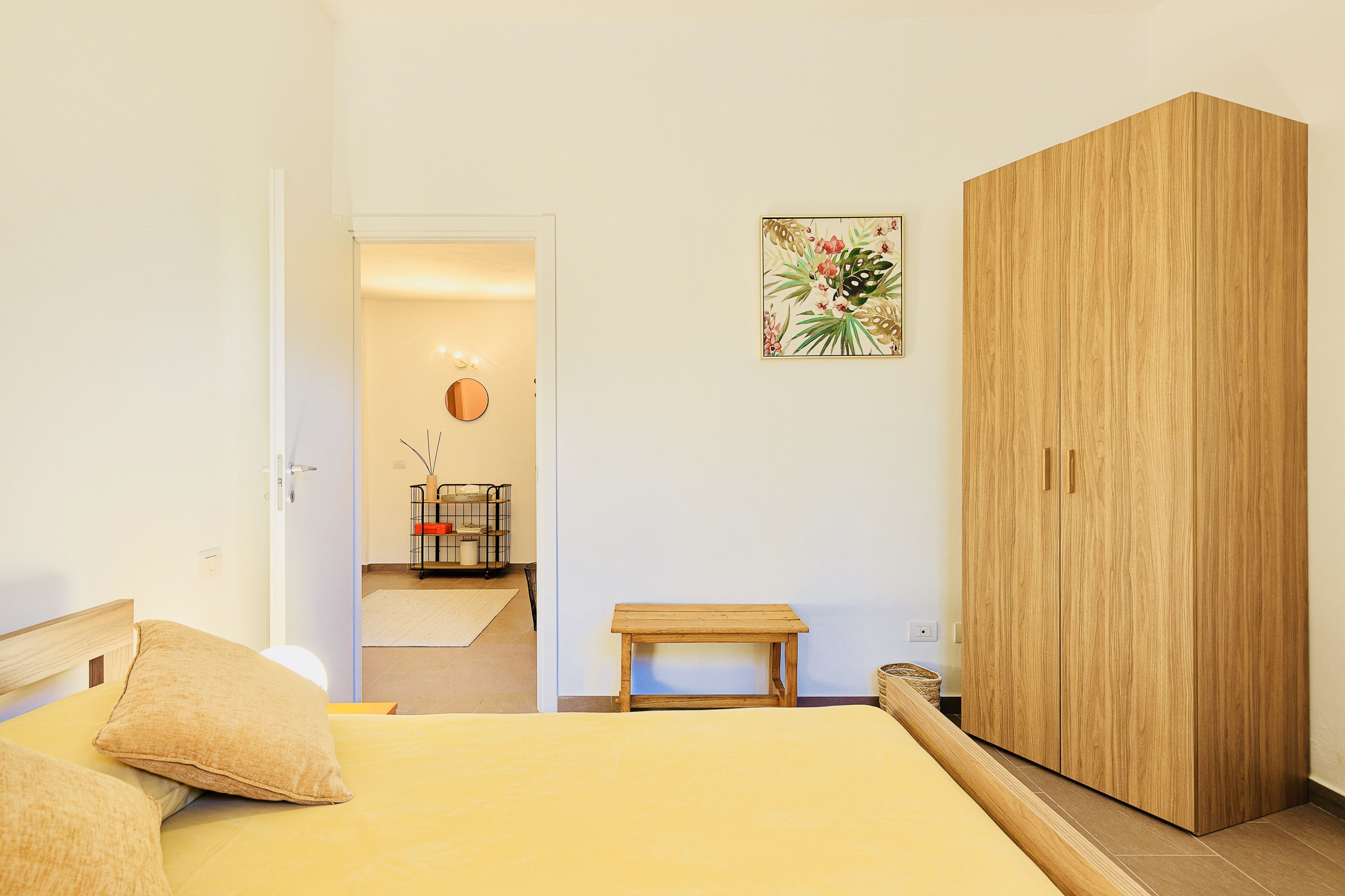 Une chambre à coucher comprenant un lit, une armoire en bois, une petite table en bois, un miroir et un tableau accroché au mur.