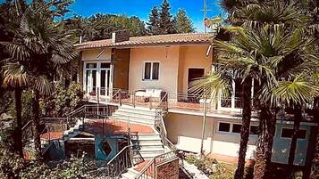 Une maison à deux étages dotée d’un balcon, entourée de palmiers et surplombant un ciel d’un bleu limpide.