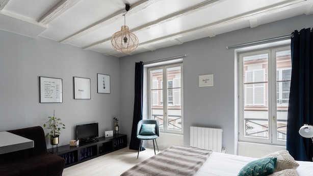 Quarto moderno com cama, escrivaninha, televisão e janela com cortinas.