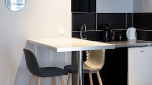 Uma cozinha moderna com bancada branca, duas cadeiras pretas, uma pequena geladeira e um exaustor preto.