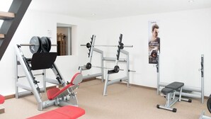 Une salle de sport équipée de matériel de musculation, d’un banc et d’une affiche au mur.