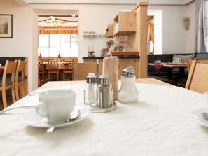 Ein Esstisch mit weißer Tischdecke, Salz- und Pfefferstreuern, einer weißen Tasse und einem Untertasse.