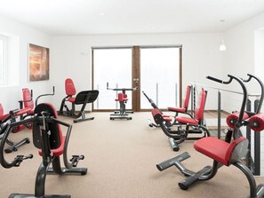 Ein Fitnessraum mit verschiedenen Trainingsgeräten, einem großen Fenster und einer Tür.