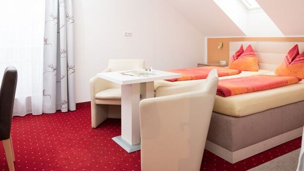 Une chambre d’hôtel avec un lit, une petite table, une chaise et une fenêtre avec des rideaux.