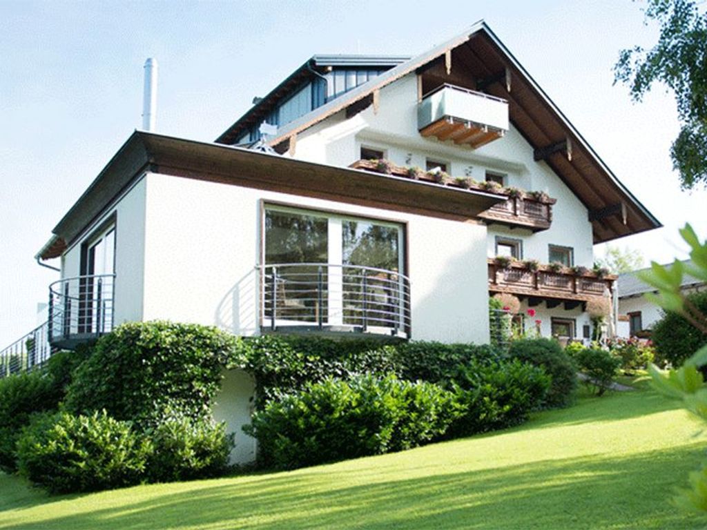 Ein modernes, zweistöckiges Haus mit Balkon, großen Fenstern und einem gepflegten Rasen.