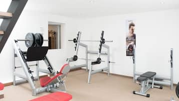 Ein Fitnessraum mit Gewichtstrainingsgeräten, einer Bank und einem Poster an der Wand.