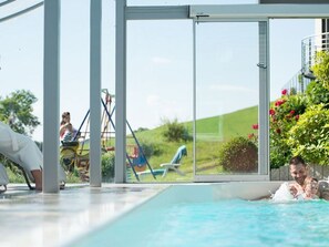 Une piscine intérieure avec des parois en verre transparent, un toboggan et une vue sur un paysage verdoyant.