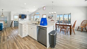 A spacious kitchen with a central island, a dining area with wooden chairs, and a large window offering a view.