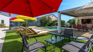 Un jardin avec une piscine, du mobilier d’extérieur et des parasols.