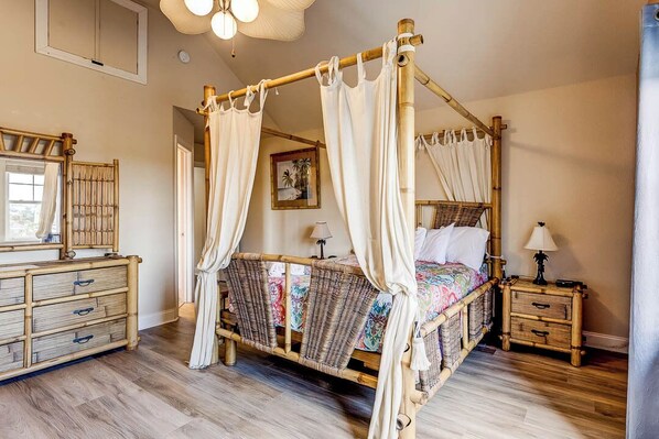 A four-poster bed with a canopy, a wooden dresser with drawers, a nightstand with a lamp, and a framed picture on the wall.