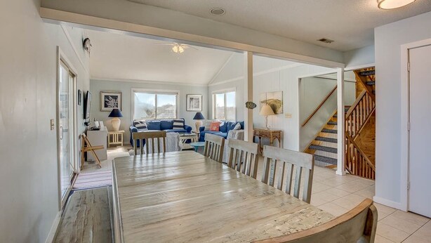 Un vaste espace de vie comprenant une grande table à manger en bois, des canapés bleus et un escalier menant à un niveau supérieur.