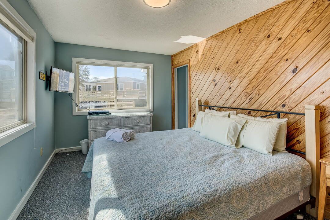 A bedroom with a bed, a dresser, a window, and a wooden wall.